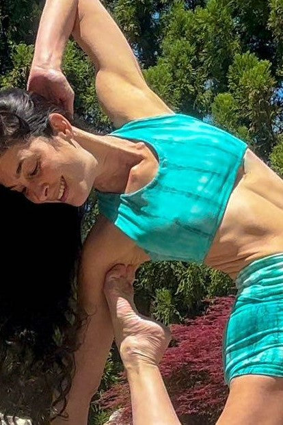 Teal tie dye sports bra with streaks of blue/green worn on woman in yoga pose. Made of 90% cotton with 10% spandex.