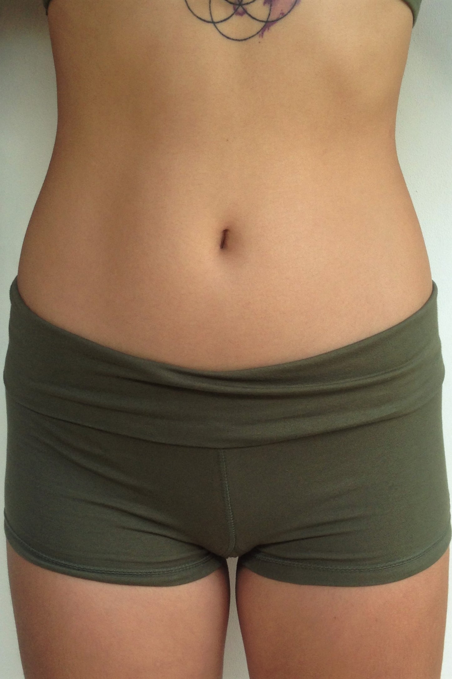 Front view solid Sage green yoga shorts with fold over waist, can be worn higher waisted, or low on the hips. Small black Lotus Flower embroidery. 90% cotton 10% spandex.