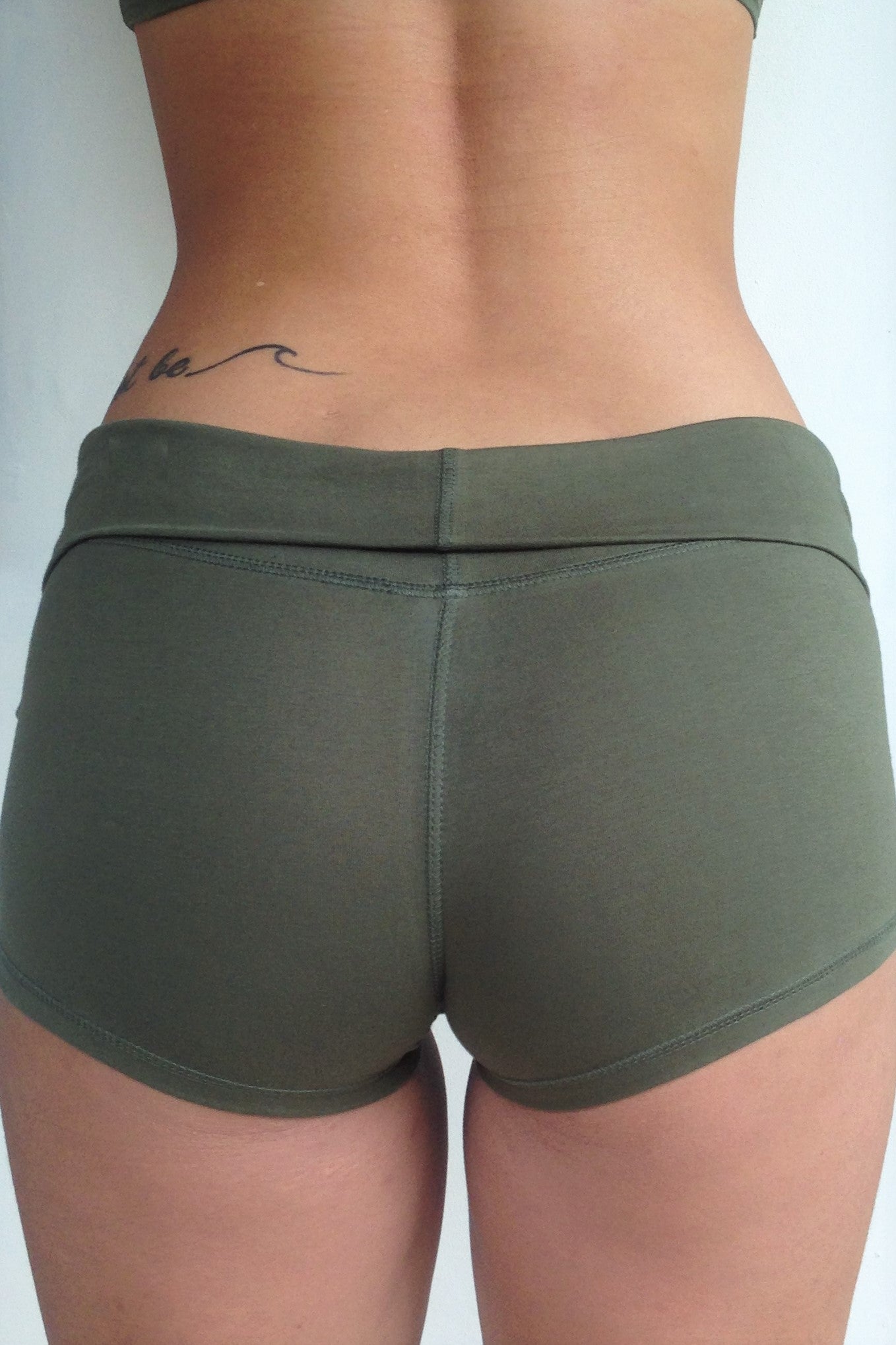 Back view of solid Sage green yoga shorts with fold over waist, can be worn higher waisted, or low on the hips. Small black Lotus Flower embroidery. 90% cotton 10% spandex.